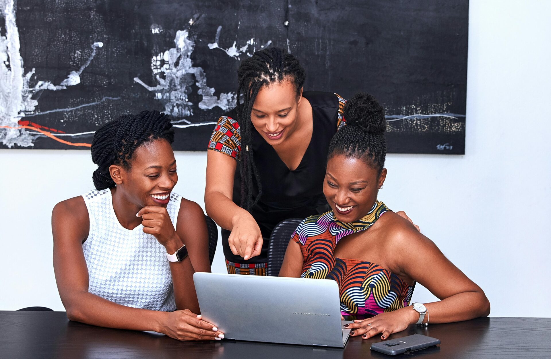 Three professional women collaborating at a laptop during a LinkedIn Ads management strategy session in a modern office setting.