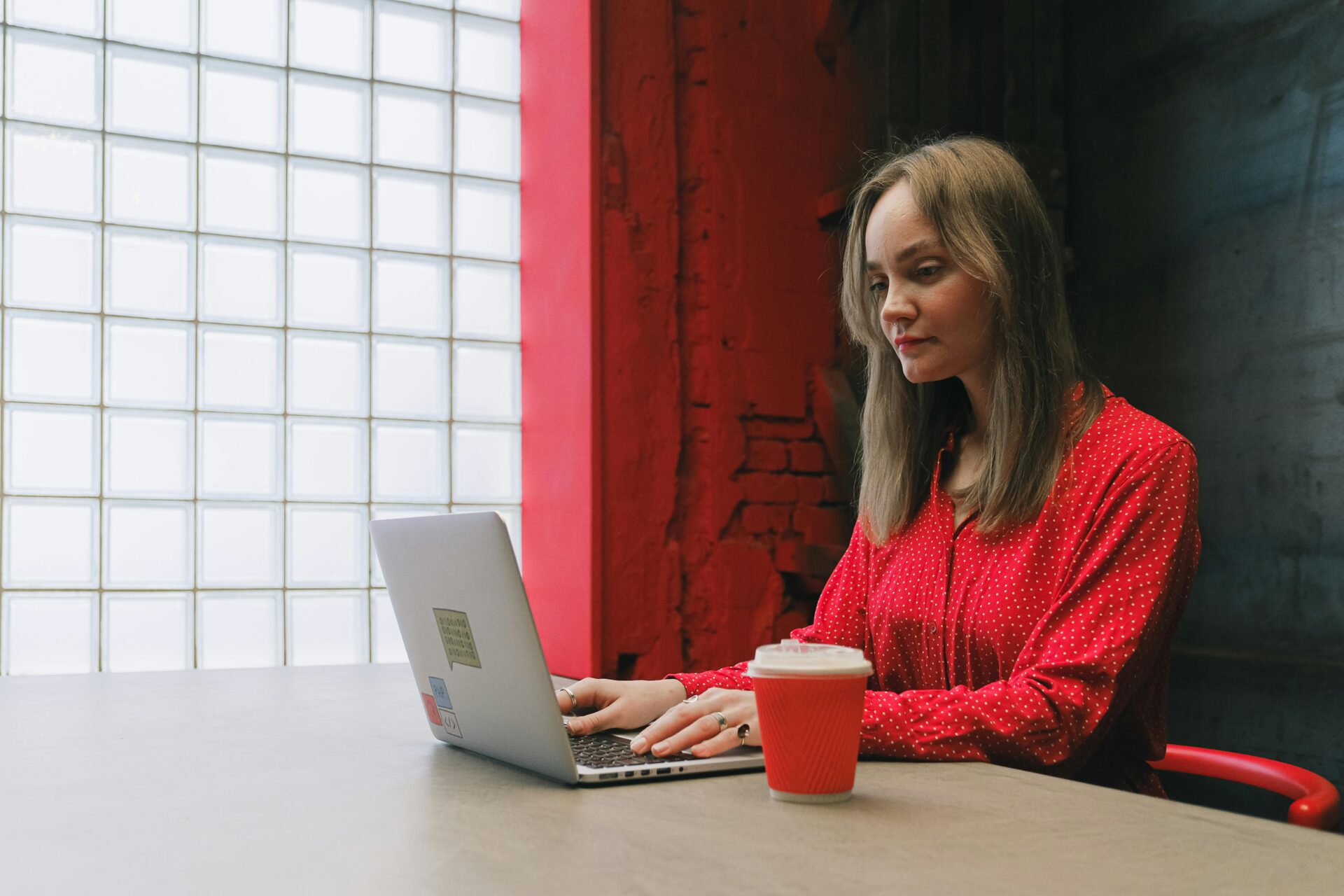 Woman in a red blouse working on a laptop in a modern office space, representing ecommerce web design concepts with a coffee cup beside her.