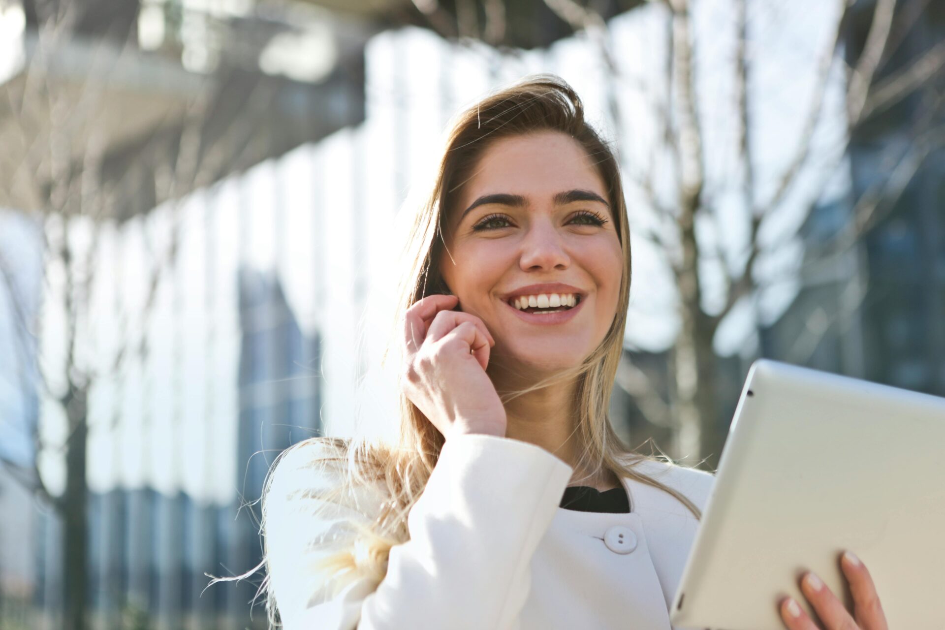 Smiling businesswoman holding a tablet and talking on the phone outside an office building, representing digital marketing and SEO for estate agents.